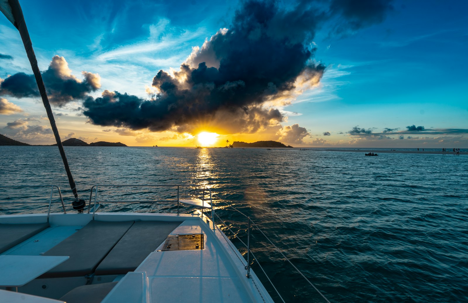 Catamaran sailing towards a vibrant sunset over the ocean.